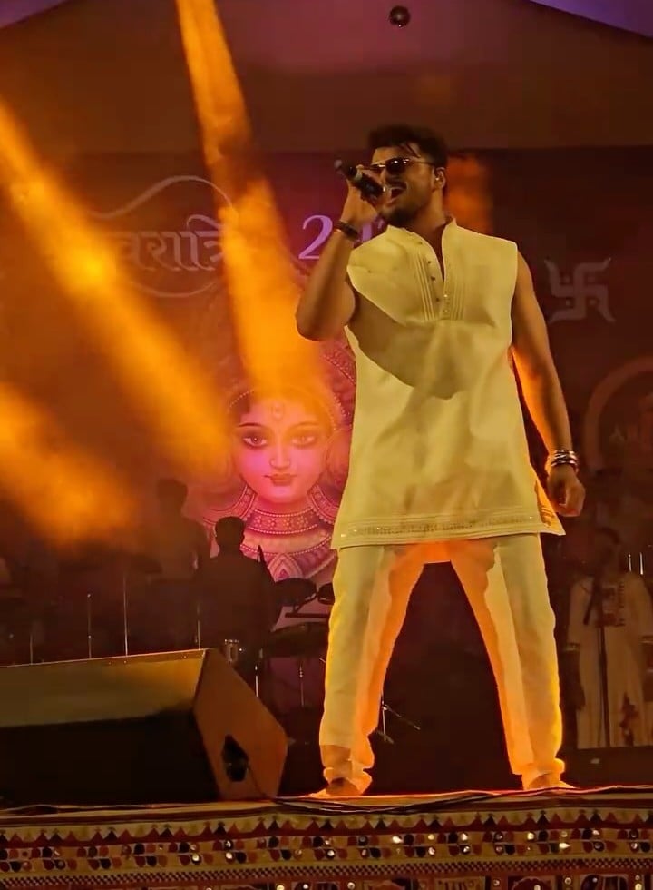 JP Kalaravkar in a cream kurta singing under amber spotlights at a Navratri 2025 performance
