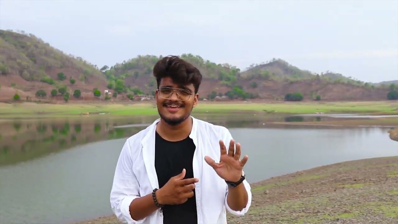 JP Kalaravkar in a white shirt singing by a lake with hills behind, from his Kahani cover
