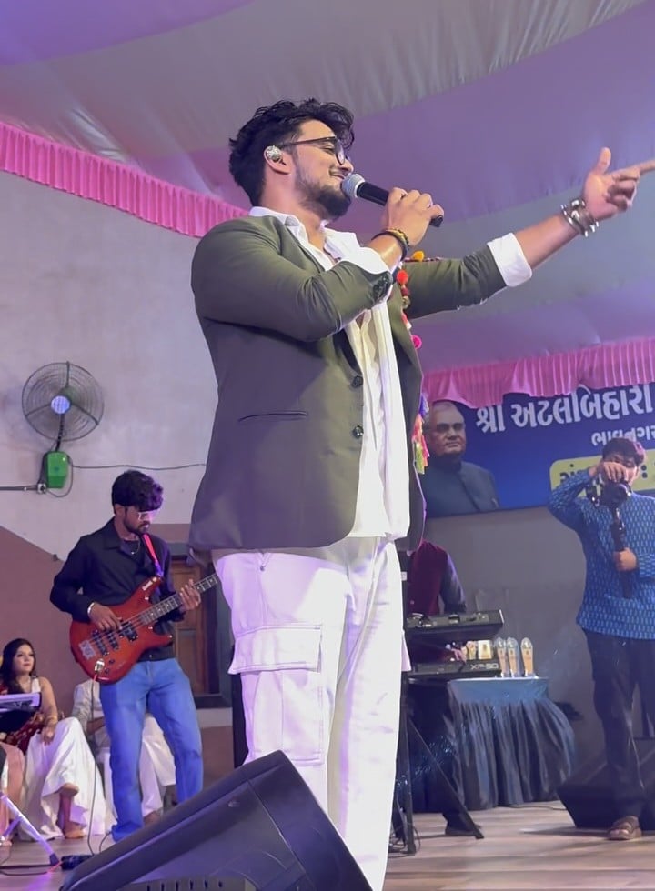 JP Kalaravkar in an olive blazer and white, singing and pointing to the crowd during Navratri 2025, a guitarist behind him