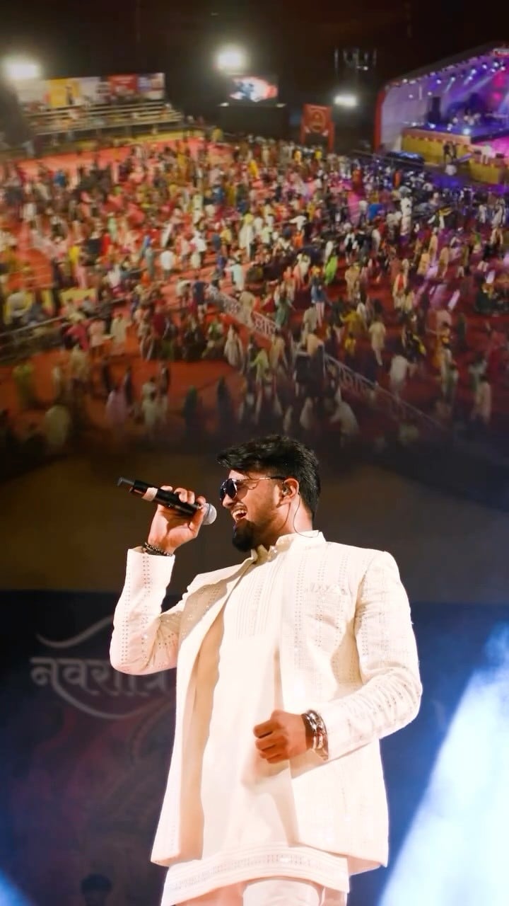 JP Kalaravkar in an ivory outfit singing on the Rajpath Navratri stage, a garba crowd filling the ground behind him